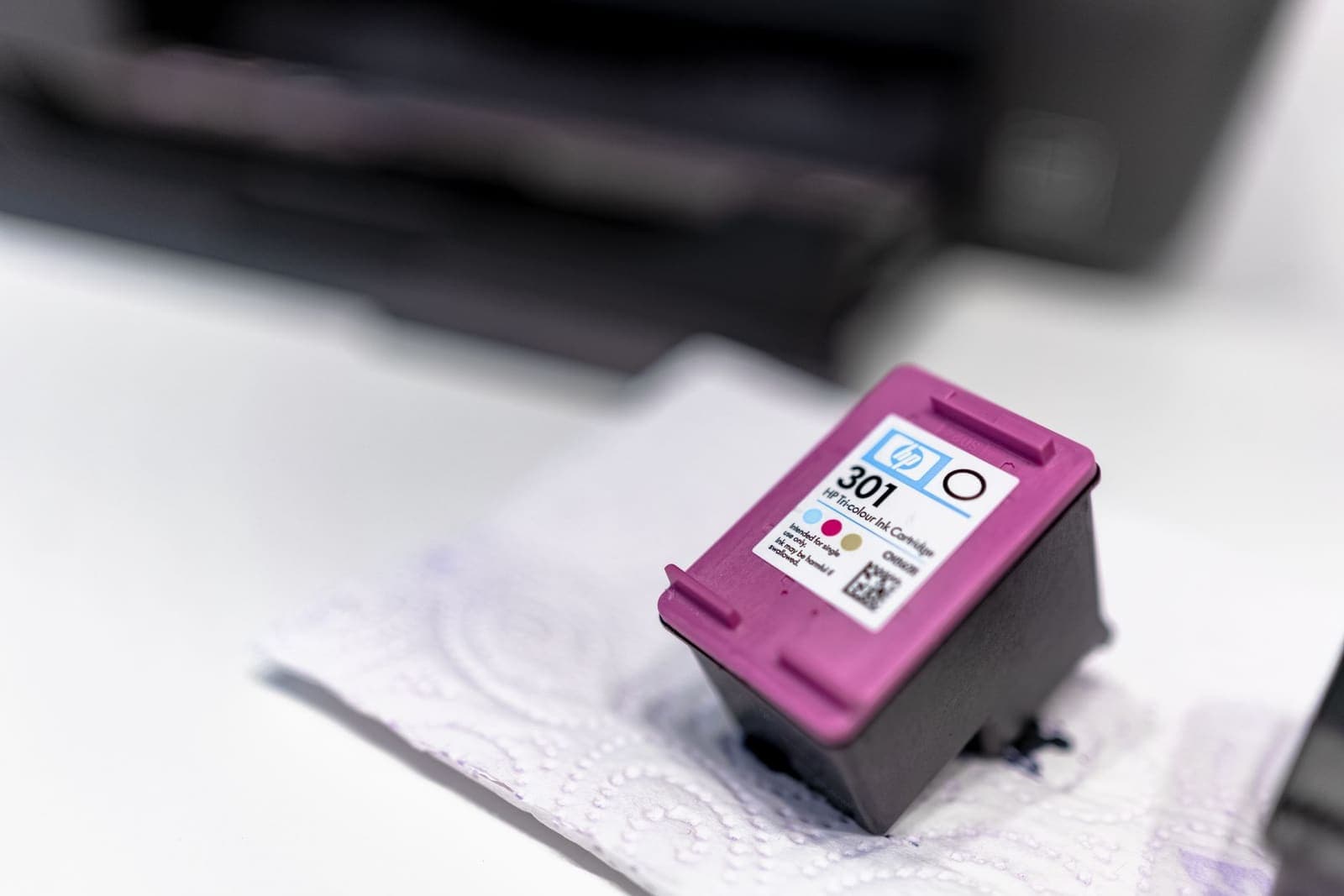 Magenta inktcartridge op een lichte doek, met een printer op de achtergrond